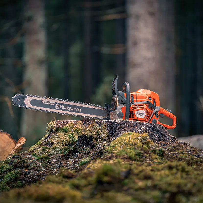 Husqvarna chainsaw on a forest floor with blurred trees in the background